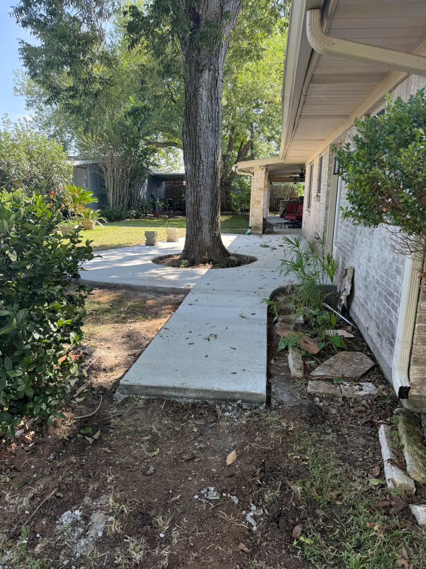 Finished concrete walkway connecting the home to a tree-centered patio