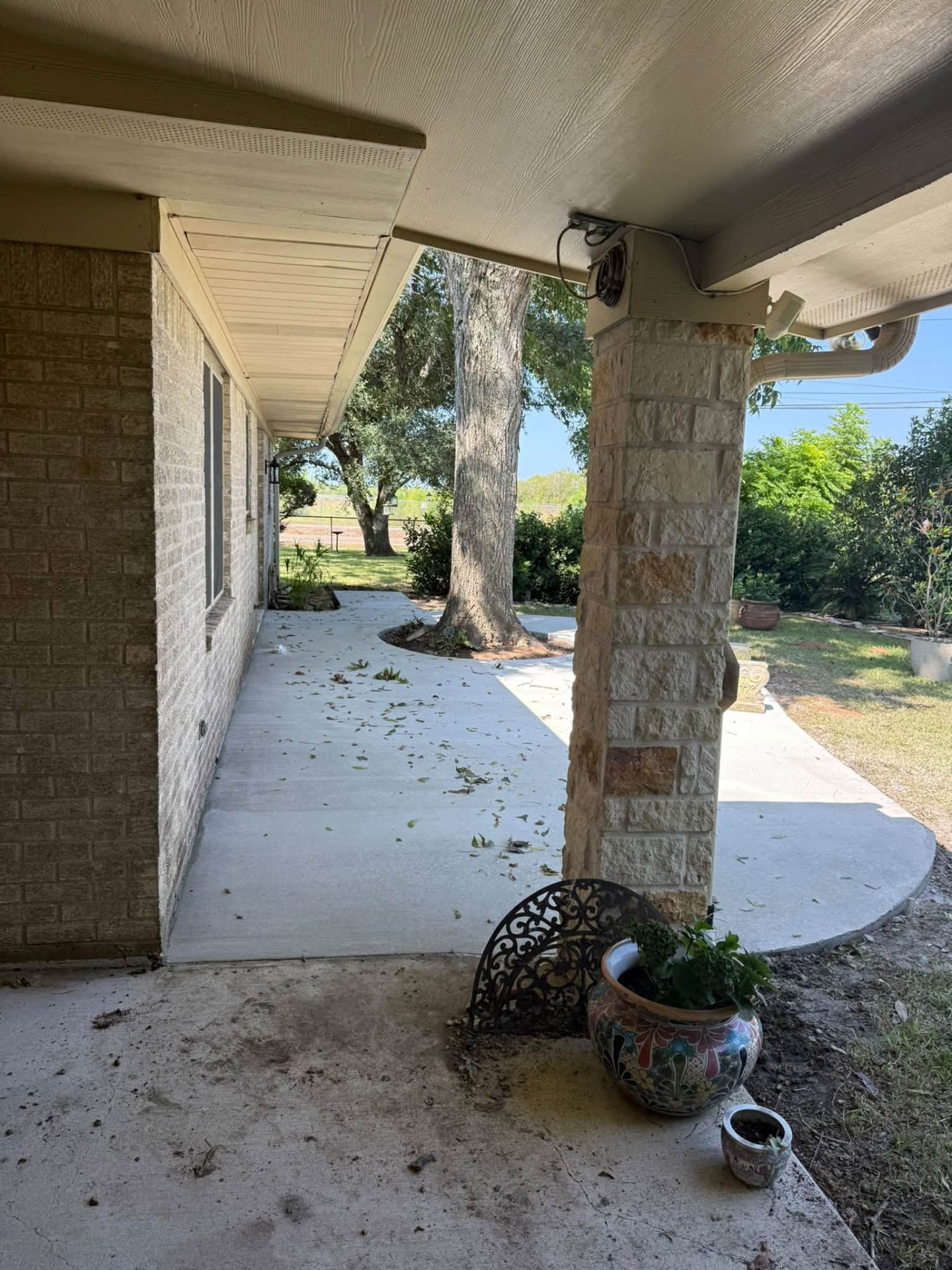 Covered view of a new concrete patio extending along a brick home and around a mature tree