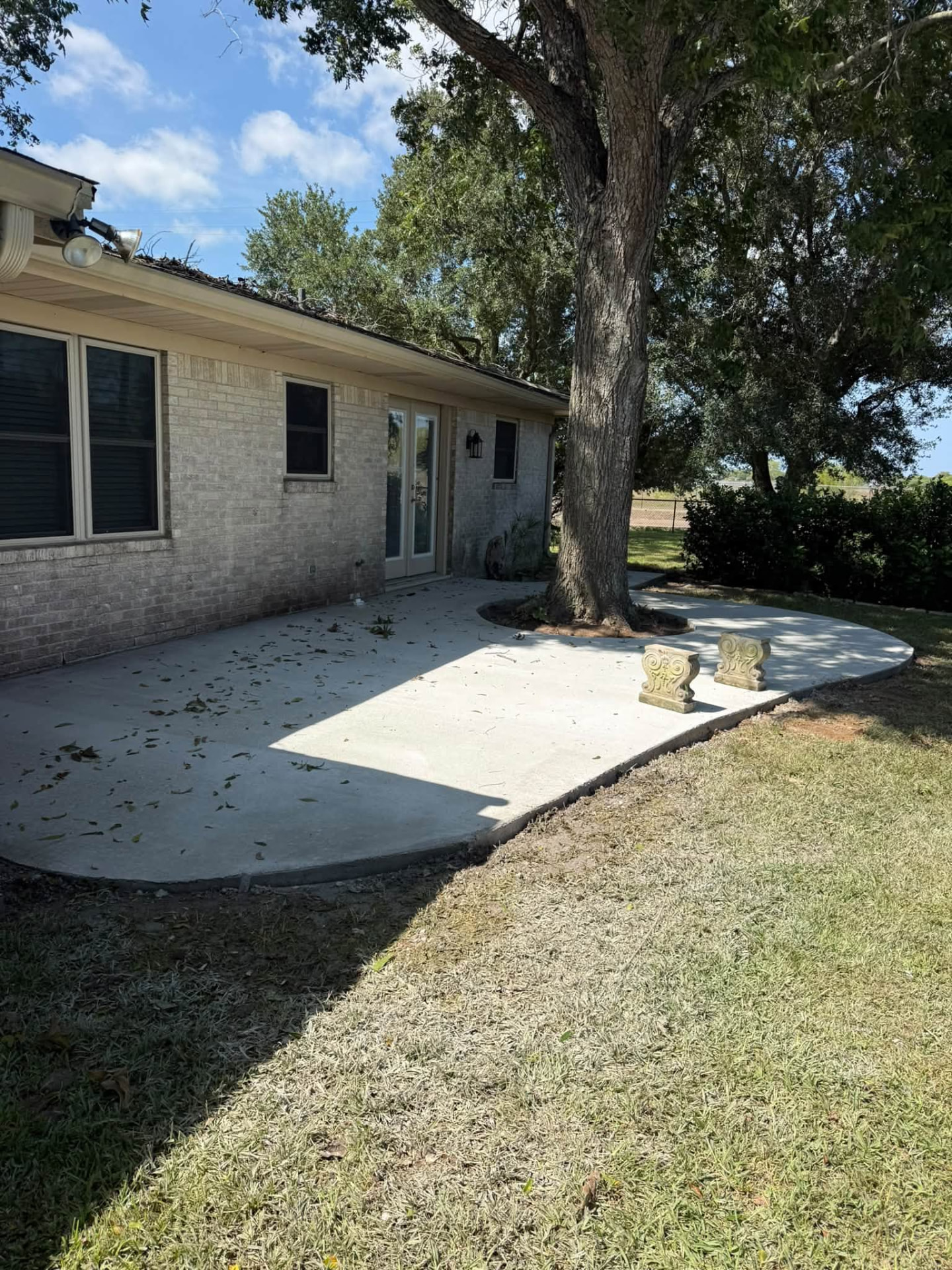 Wide view of a finished concrete patio shaped around a mature tree beside a brick home