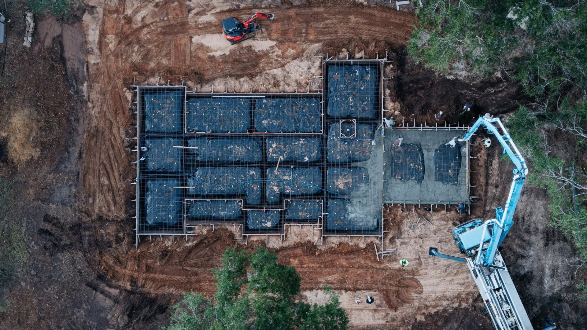 Direct overhead view of reinforced foundation formwork during concrete placement