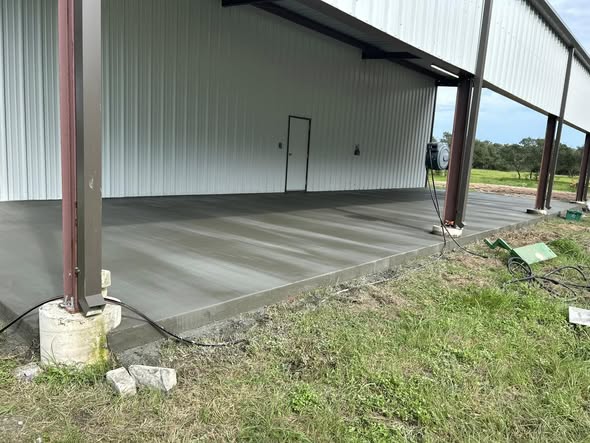 Freshly finished concrete slab beneath an open-sided metal building